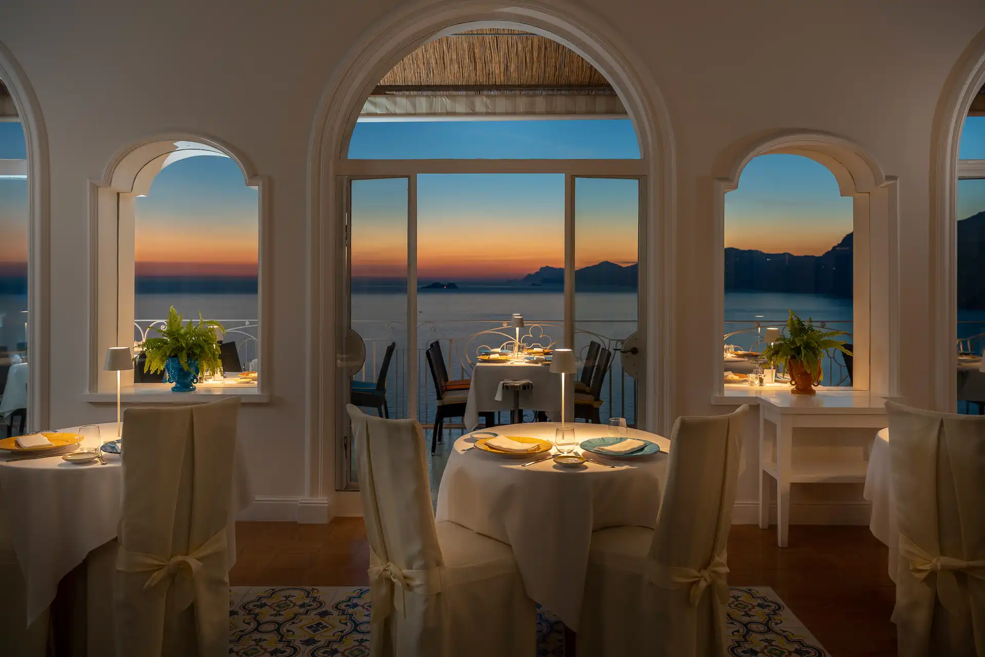 Ristorante elegante con vista sul tramonto marino attraverso vetrate ad arco.