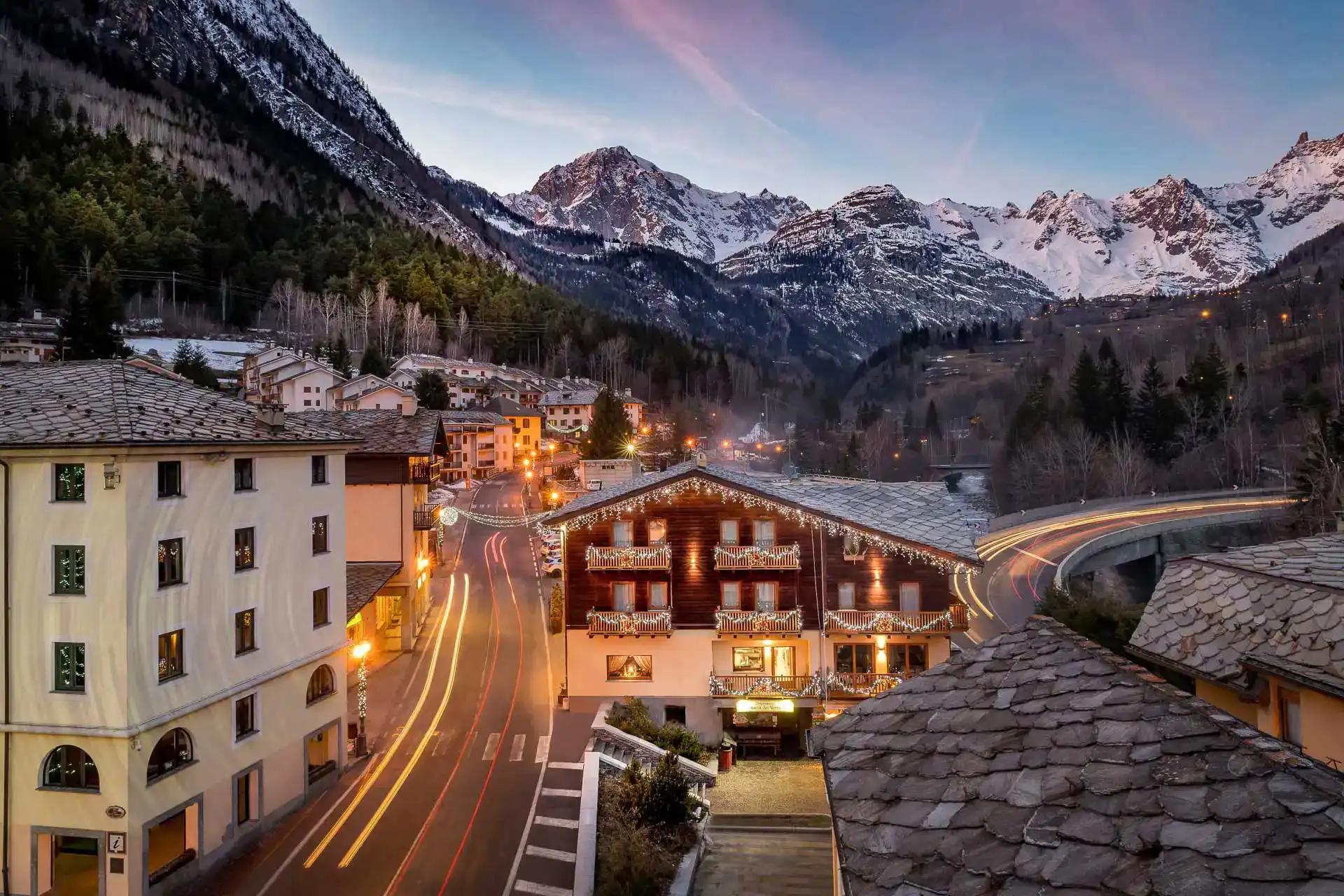 Veduta di un pittoresco villaggio alpino illuminato al tramonto, con montagne innevate sullo sfondo.