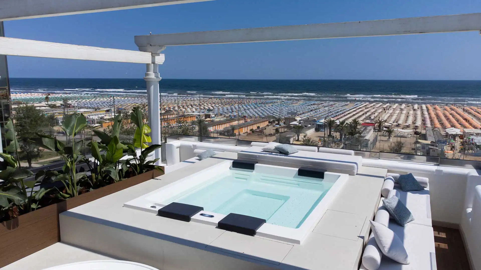 Terrazza con vasca idromassaggio affacciata su una spiaggia piena di ombrelloni colorati.
