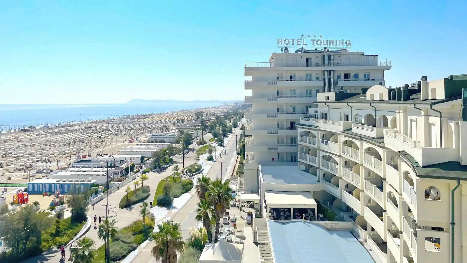 Vista aerea di un grande hotel fronte mare con spiaggia affollata a lato.