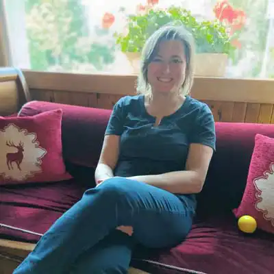 Donna sorridente su un divano rosso con cuscini decorati.